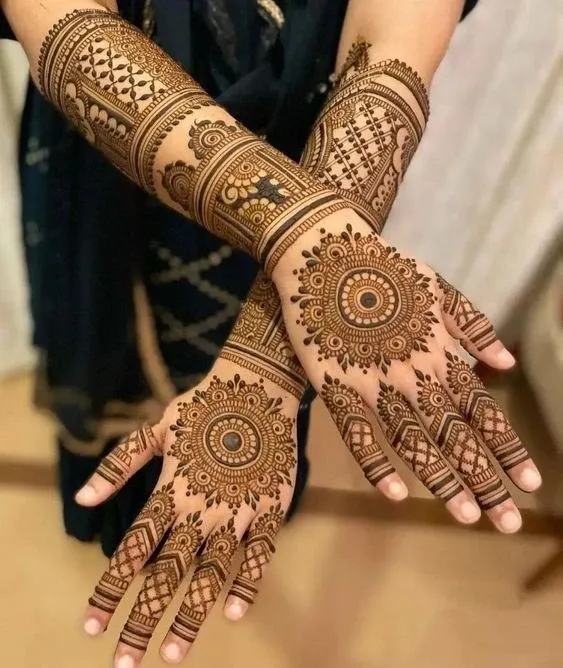 A stunning symmetrical mandala mehndi design on both hands, extending up the forearms. The clean, intricate patterns and dark henna stain create a classic and elegant look perfect for a bride.