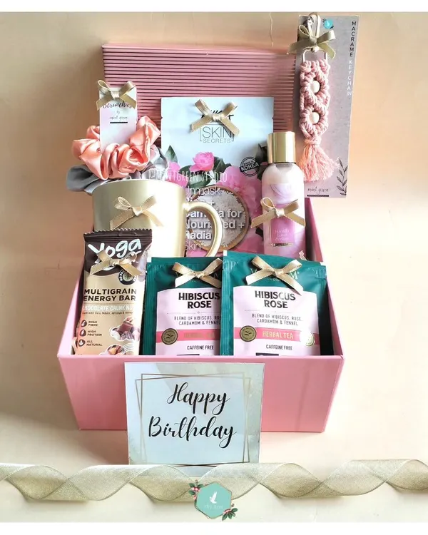 A birthday hamper designed to pamper. This pink-themed box includes hibiscus rose tea, a multigrain energy bar, a face mask, a personalized mug, and other self-care goodies.