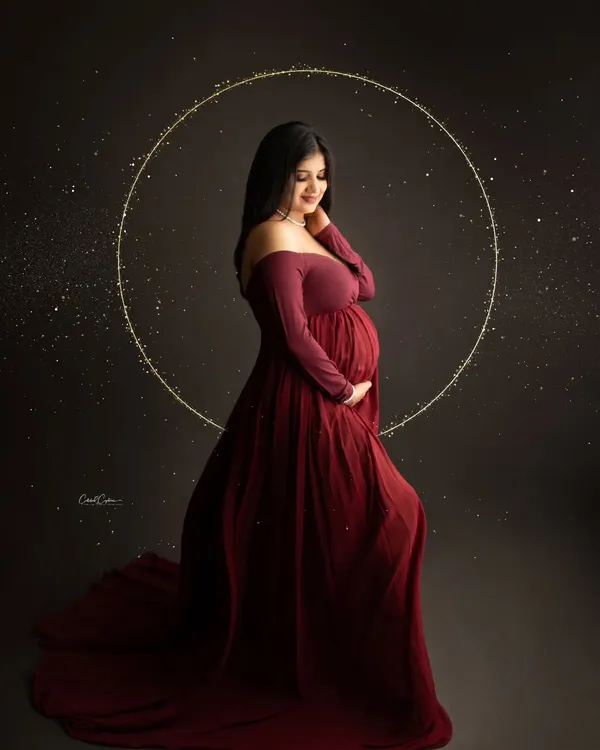 A magical and elegant portrait. The mom-to-be is framed by a glowing halo, her deep red gown and the sparkling lights creating a celestial feel.