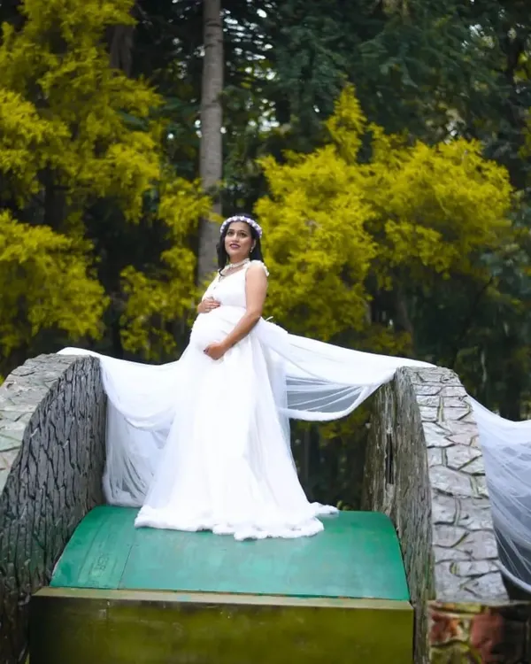An expecting mother looking serene on a bridge, wearing my flowing white maternity gown. The long trail adds a touch of drama to this beautiful outdoor nature shot.