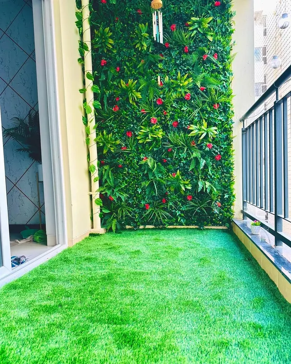 A perfect example of a vibrant balcony transformation. We used a mix of broad leaves and small red flowers for the vertical garden, paired with our durable artificial grass, to create a lively and comfortable outdoor living area.