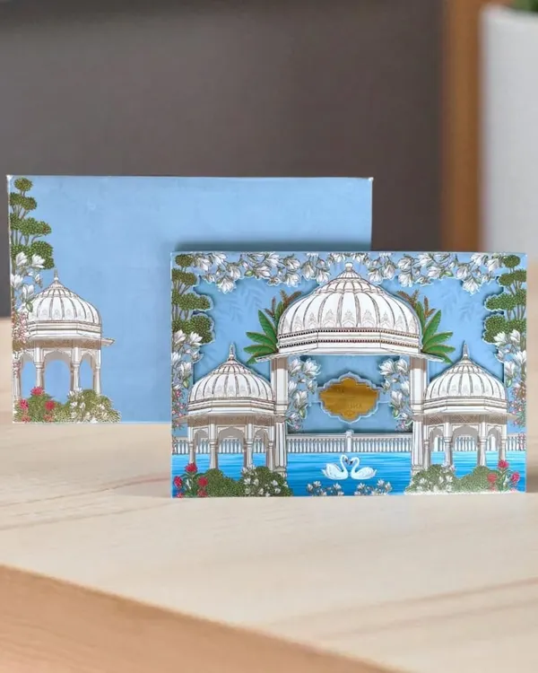 This Pichwai-themed card features serene white gazebos and swans against a sky-blue background, offering a peaceful and artistic announcement for your wedding.