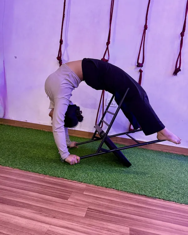 Using a chair to support a deep backbend. This prop helps open up the thoracic spine safely, allowing for a greater range of motion in Urdhva Dhanurasana.