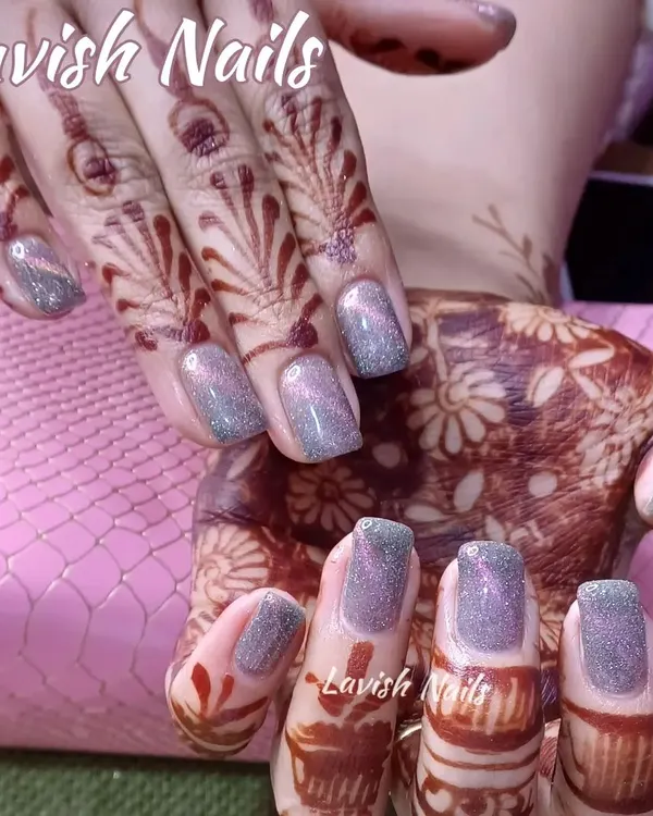 A set of square-shaped nails with a shimmering, color-shifting glitter polish that contrasts beautifully against intricate bridal mehendi designs.