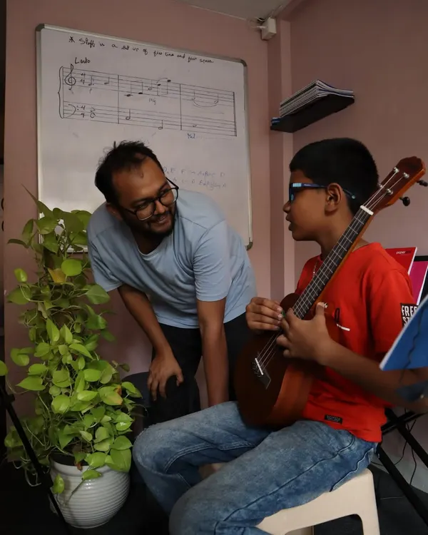 A perfect moment of mentorship. Our instructor guides a young ukulele student, with music theory visible on the whiteboard behind them.