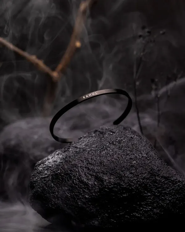 For this custom men's bracelet, I created a dark, moody atmosphere using a natural rock and subtle smoke. This dramatic lighting highlights the matte black finish and personalized engraving, giving the piece a powerful and luxurious feel.