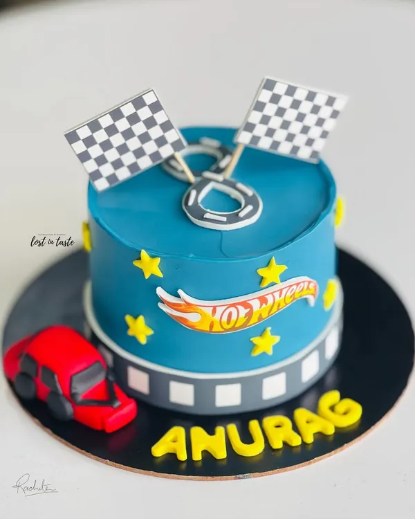 A Hot Wheels themed cake for a young racing fan. This design features a vibrant blue buttercream, the Hot Wheels logo, checkered flags, and a toy car.