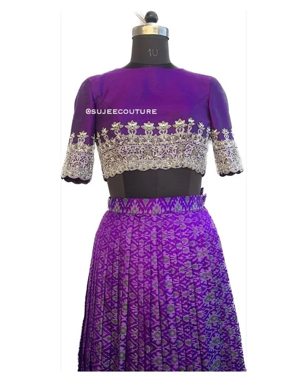 A full view of the custom purple Ikkat lehenga set on a mannequin. The outfit includes a pleated lehenga skirt and a raw silk blouse with intricate silver hand embroidery on the sleeves and hem.