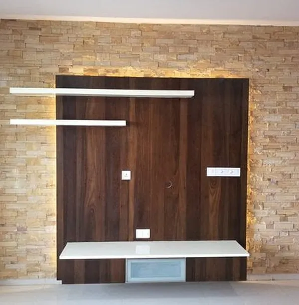 A custom TV unit featuring a dark wood back panel set against a stone-cladding wall. The floating white shelves and console create a modern, airy feel with integrated backlighting.