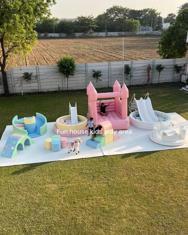 An expansive outdoor party setup featuring our diverse rental attractions. This arrangement includes a pink bouncy castle, a pastel soft play area with a ball pit, and an elegant white play zone with a slide and merry-go-round, showcasing how we can fill any large space with a variety of fun for all ages.