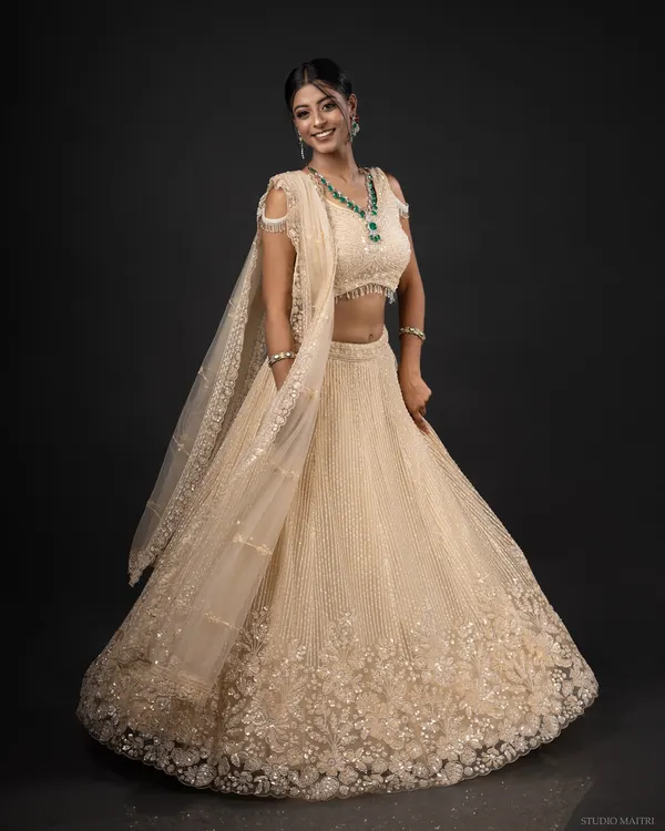 A joyful, full-length shot of a model in a stunning cream and gold lehenga, complete with an emerald jewellery set. This captures the grandeur of modern Indian bridal fashion.