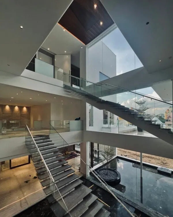 An orchestration of scale, light, and void. This multi-level floating staircase with glass railings creates a sense of transparency and elegance, connecting floors while allowing light to filter through the entire home.