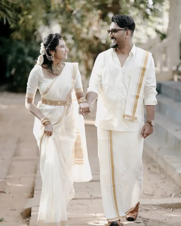 An elegant walking shot of a couple in traditional Kerala attire, a white mundu and saree, capturing a moment of grace and cultural pride.