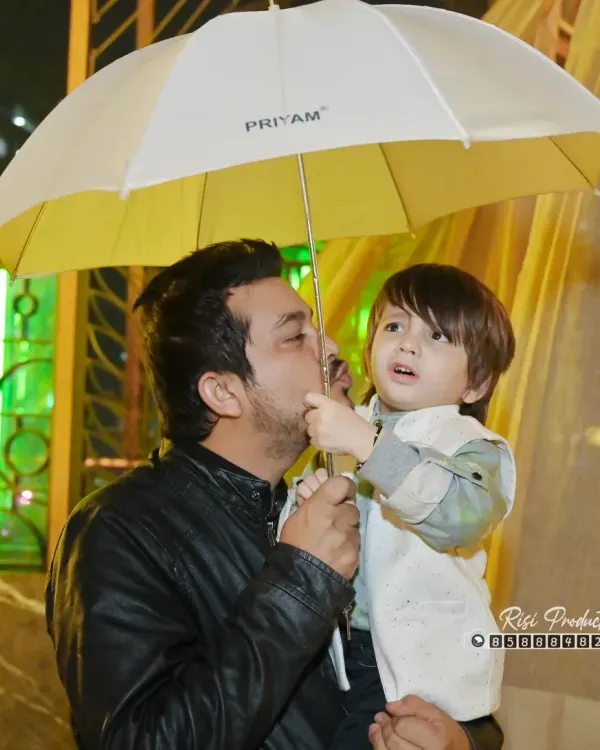 A tender moment between a father and son, sheltered under an umbrella. This artistic shot beautifully captures the protective and loving bond they share.