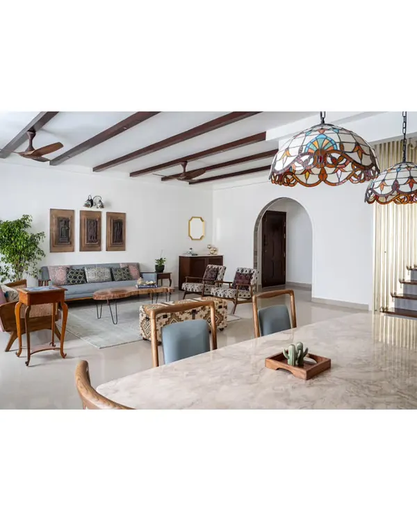 The open-plan living and dining area of our 'Spanish Country Home' project. Walnut-hued wooden rafters span the ceiling to conceal wiring and add vintage allure, while distinct furniture groupings and rugs delineate the spacious layout.