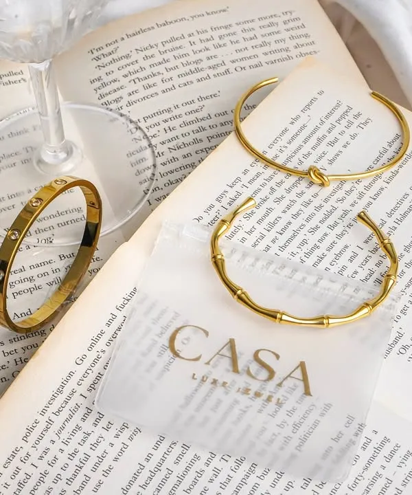 An aesthetic flatlay of gold bracelets styled on an open book with a wine glass. This type of editorial product photography is perfect for creating a sophisticated and literary brand image.