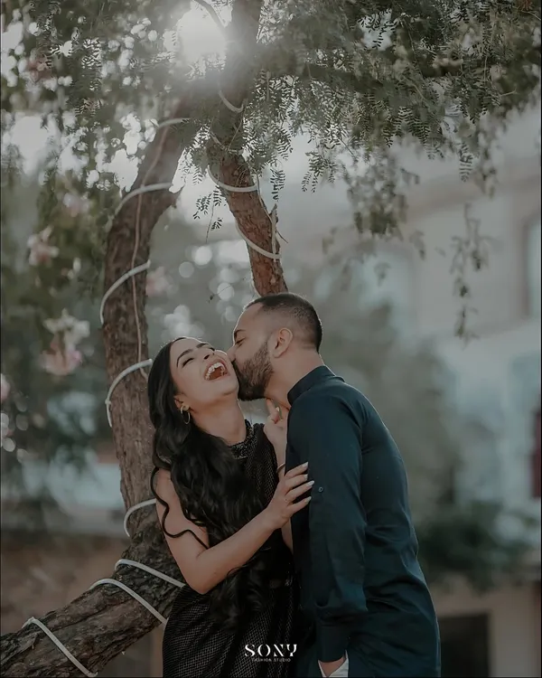 The perfect candid shot. The groom's kiss on her cheek elicits a burst of genuine laughter from the bride, capturing a moment of pure, unscripted happiness.