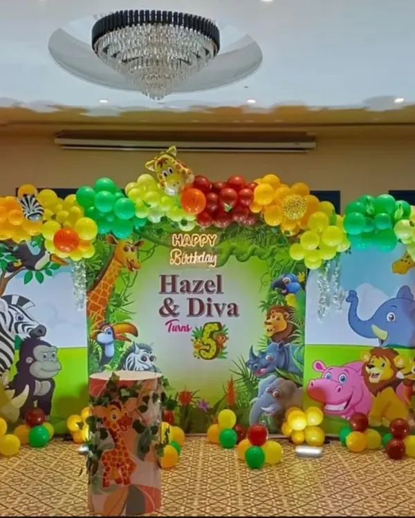 A vibrant and classic jungle theme stage setup for Hazel & Diva's 5th birthday. This backdrop is filled with friendly jungle animals and surrounded by a colorful balloon arch.