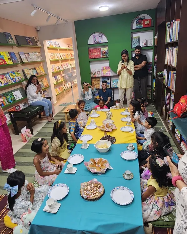 Welcome to a birthday party where stories come to life. Here, children are gathered for a delightful Mrs. Potts' Tea Party, seated at a long table surrounded by bookshelves filled with adventures waiting to be read.