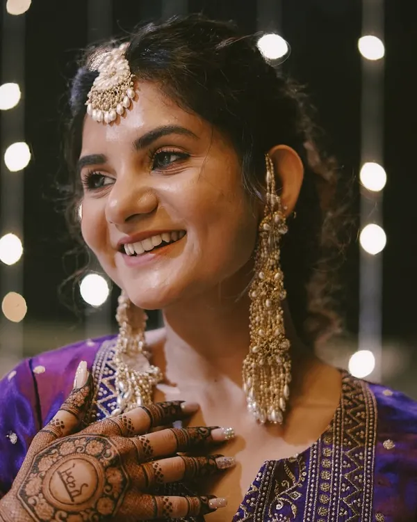 A happy client smiling through her Mehendi ceremony. We customized these iconic pearl tassel earrings and a matching bindiya to complement her vibrant purple outfit, creating a look that's both classic and full of personality.