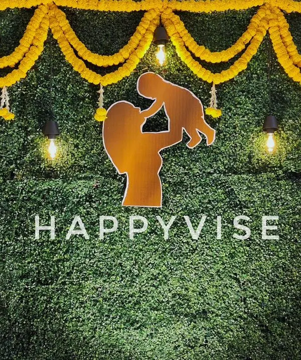 A modern take on Haldi decor, this backdrop features a green foliage wall decorated with marigold garlands. The silhouette of a mother and child adds a personal, heartwarming touch.