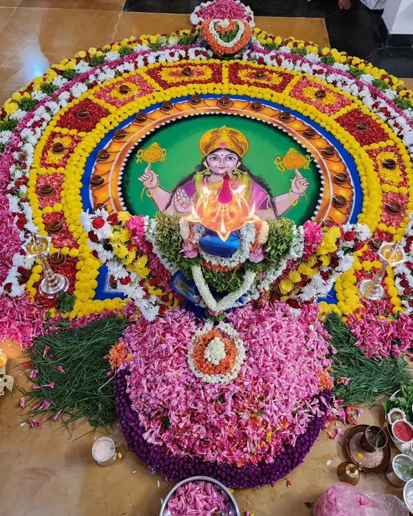 A grand and vibrant rangoli for a Durga Deepa Namaskara pooja. The depiction of the Goddess is surrounded by layers of fresh flower petals and a circle of lamps, creating a truly magnificent sight.