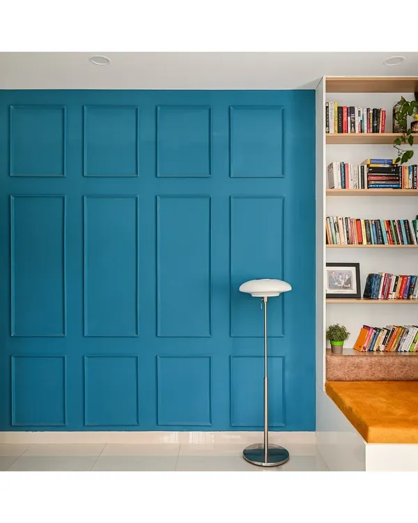 I designed this cozy reading corner to be a perfect escape. It features custom-built corner shelves for an extensive book collection and a comfortable cushioned seat, set against a bold blue paneled accent wall.