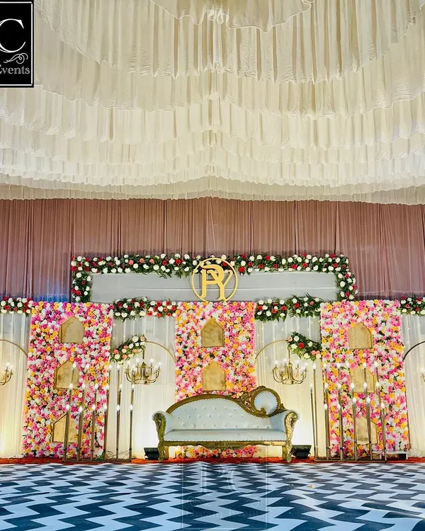 A full view of a grand wedding stage. I used a striking black and white chevron floor, a massive floral wall with alcoves, and a royal white sofa to create a high-impact, glamorous look.