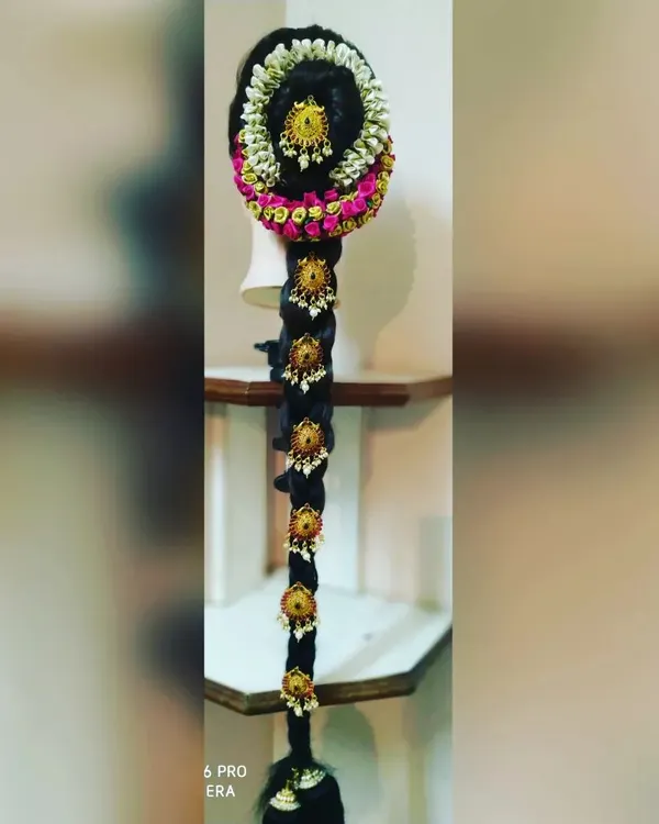 A full view of a traditional 'poola jada' hairstyle for a bride. The long braid is heavily adorned with jasmine flowers and gold ornaments, creating a grand and customary look for a muhurtham ceremony.