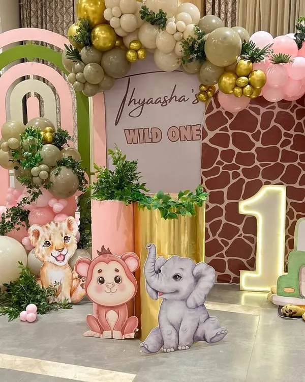 We brought this personalized "Wild One" jungle theme to life for a first birthday party. This setup features custom character cutouts of a giraffe, lion, and elephant, a large name backdrop, and a multi-colored balloon arch in sage green, pink, and gold.