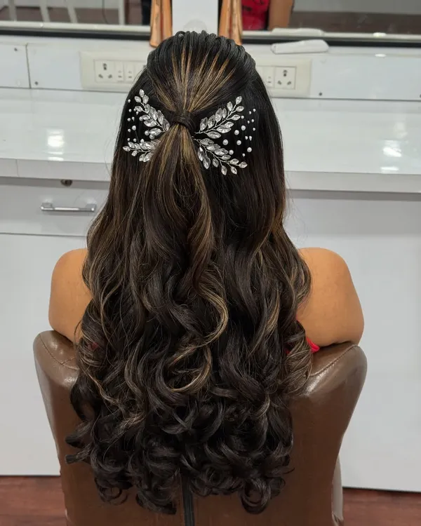 A modern and chic hairstyle for a reception or sangeet. This half-up style with soft curls is accented with a beautiful crystal bow clip.
