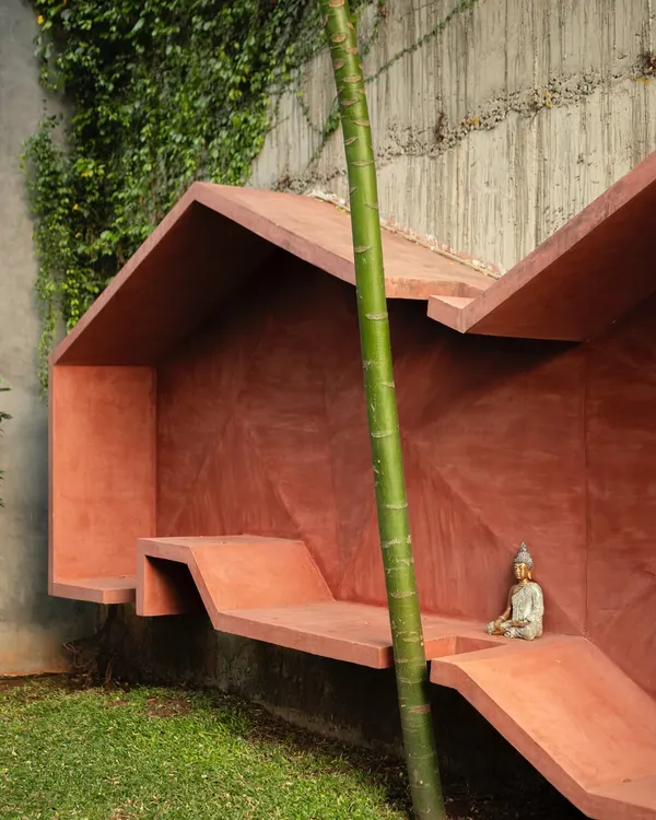 A bold, monolithic seating structure in a striking red oxide finish. Tucked against a vine-covered wall, this piece blurs the line between sculpture and functional bench, creating a quiet moment of stillness in the garden.
