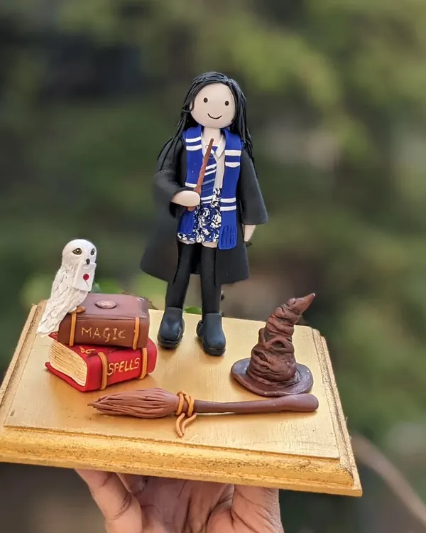 Indulge in some Harry Potter magic. This cake topper was for a special girl's birthday, and it was the fifth consecutive year I've had the honor of creating a topper for her celebration. It features a custom figurine, Hedwig, spell books, a broom, and the sorting hat.