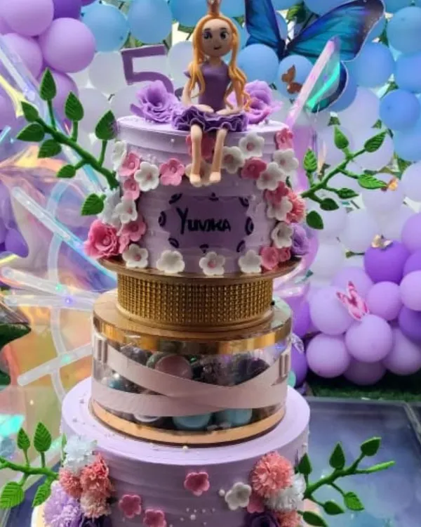 This stunning multi-tier cake features a princess topper, delicate flowers, and a transparent tier filled with macarons. The large, iridescent fairy wings add a magical touch, making it a showstopper for a 5th birthday.