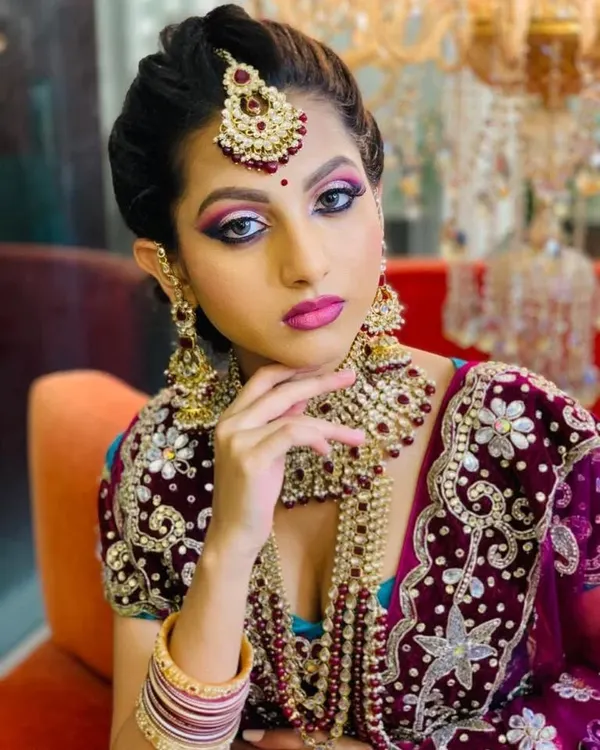 A regal North Indian bridal look featuring a dramatic smokey eye with a pop of pink and purple. The makeup is paired with heavy kundan and pearl jewellery for a truly royal feel.