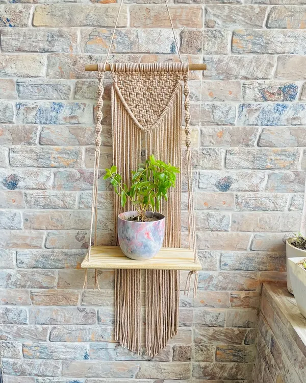 This single-tier hanging shelf features a V-shaped macrame panel with long fringe, crafted in a neutral beige cord. It’s a versatile design that fits beautifully in rustic, boho, or minimalist spaces, perfect for displaying a small potted plant.