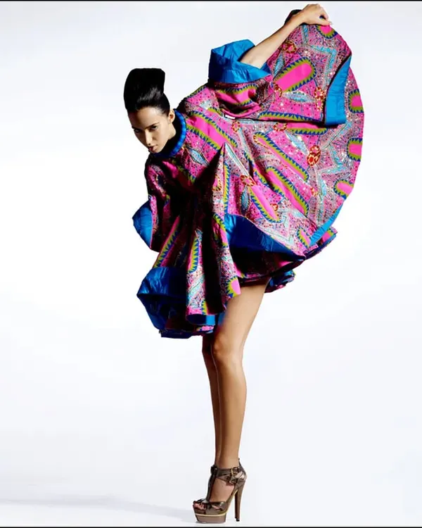 A high-fashion editorial shot for Harper's Bazaar. The model's dynamic pose and the flowing, colorful fabric create a sense of movement and sculptural beauty against a clean white background.