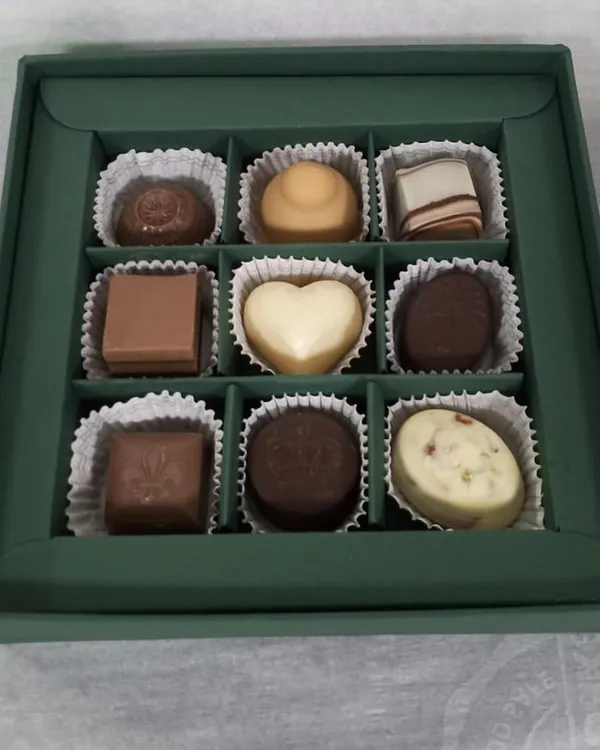 Inside a custom 9-piece box, you can see a variety of my handmade chocolates. This assortment includes a white chocolate heart, milk chocolate squares, and dark chocolate truffles, showcasing the different shapes and types I offer.