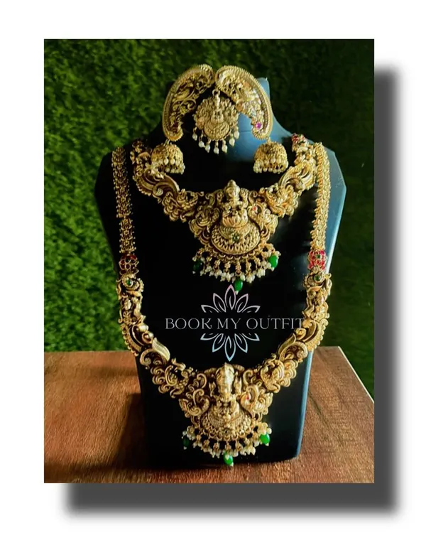 This is one of our most popular rental pieces for brides. It’s a complete, heavy temple jewelry set with intricate carvings, a layered long necklace, a matching choker, and jhumka earrings, all in a classic antique gold finish.