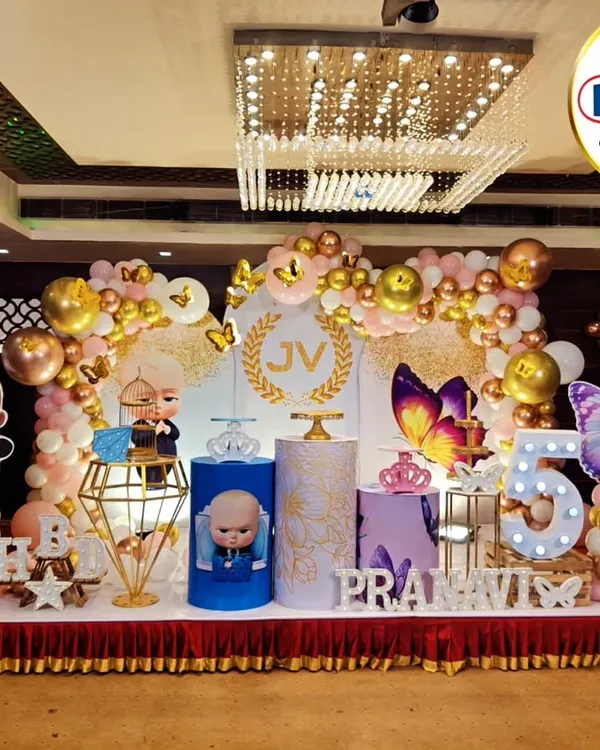 A grand and glamorous setup for a joint celebration, combining a Boss Baby theme with elegant butterflies. This stage features a sparkling gold and pink balloon arch, custom-printed backdrops, and marquee lights, showing how we can merge two distinct themes into one cohesive and beautiful design.