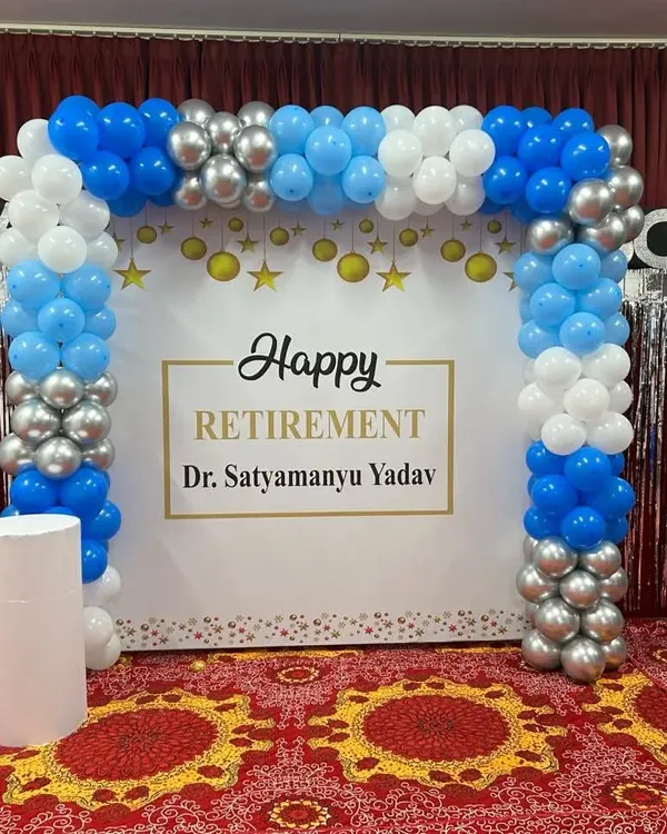 A beautiful setup for a retirement party. This decoration features a custom 'Happy Retirement' backdrop framed by a blue, white, and silver balloon arch.