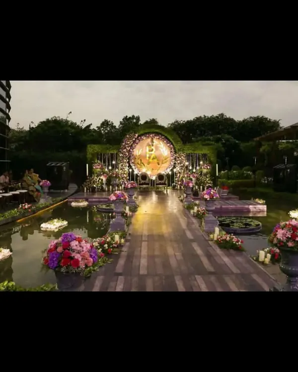 A truly magical wedding ceremony setup over a serene water body. This destination wedding design features a floating walkway, lush floral arrangements, and a stunning circular mandap, creating an unforgettable experience as dusk settles.