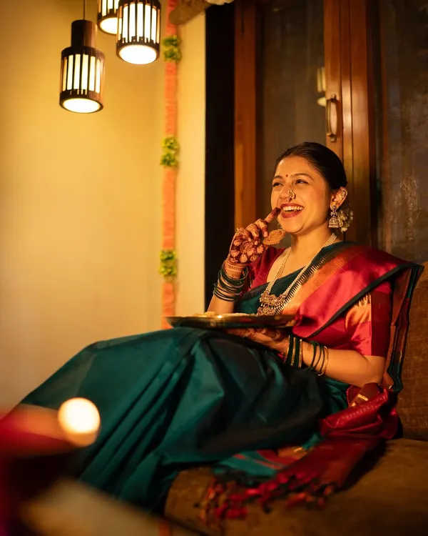 A candid shot of pure laughter during a Diwali photoshoot. Dressed in a beautiful teal and red saree, she enjoys a piece of 'faral', perfectly capturing the happy and relaxed atmosphere of the festival of lights.