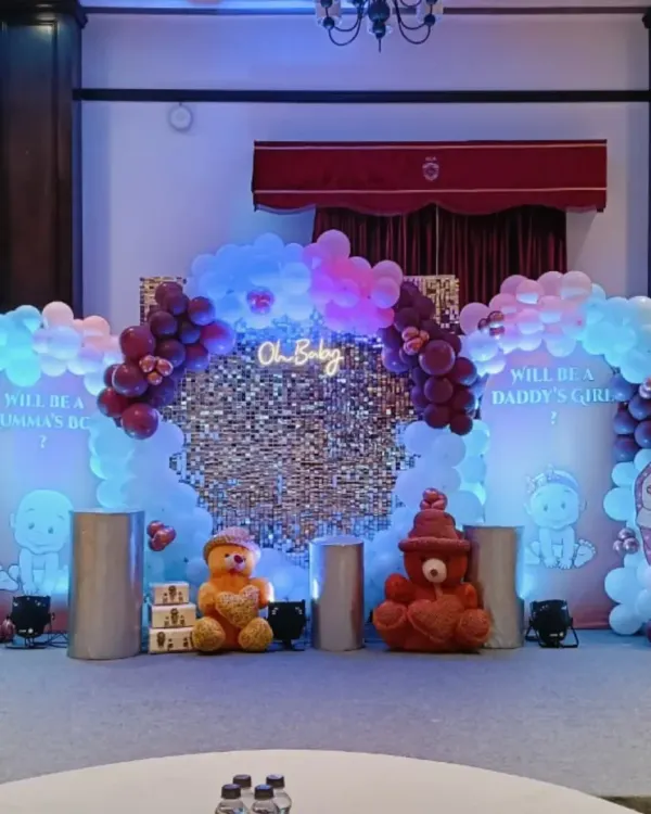 A modern 'Oh Baby' themed decoration for a gender reveal party. The setup includes a silver sequin wall, a neon sign, and balloon arrangements in pink and blue on either side.