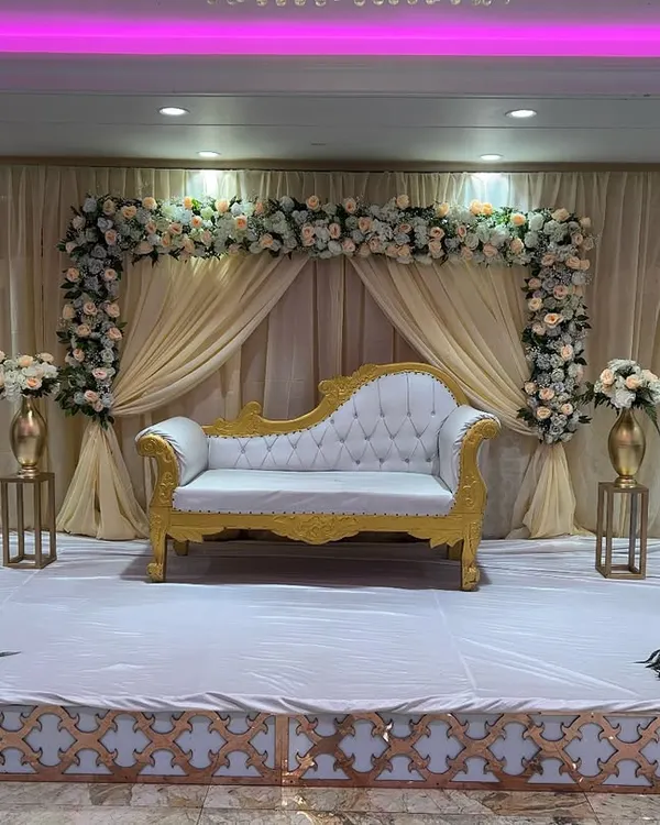 A classic and elegant stage for a reception or engagement. I used a beautiful white and gold Diwan sofa, a backdrop of cream-colored drapes, and a floral arch with white and peach roses.