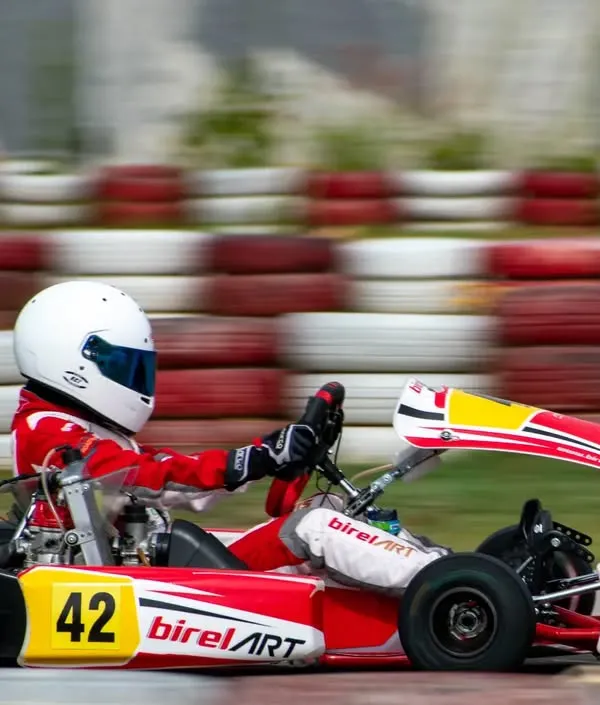 A driver in our Birel ART kart executes a turn with precision, showcasing the vehicle's agility and grip. The motion blur in the background emphasizes the high speed of competitive karting.