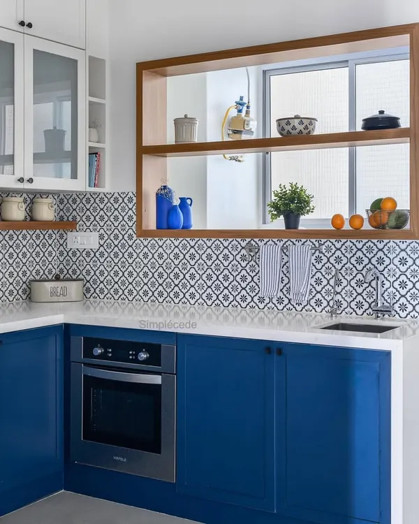 This Parisian-inspired kitchen features royal blue base cabinets and white overhead units, complemented by patterned backsplash tiles. A custom wooden frame around the utility window adds a warm, classical touch.