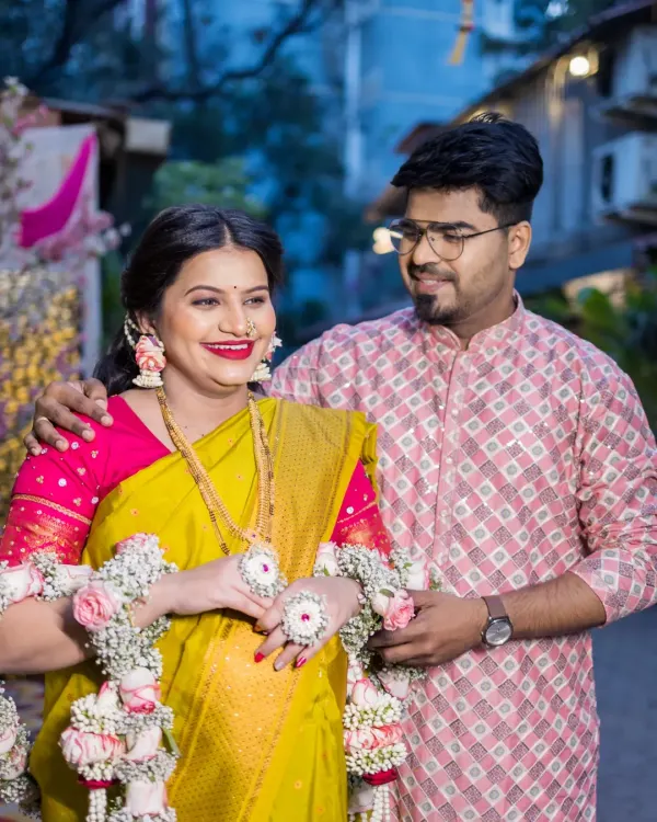 A candid, loving moment between the expecting couple during their outdoor baby shower celebration. The partner gently holds the mother-to-be, who is glowing in a yellow saree and floral jewelry, sharing a happy, private glance.