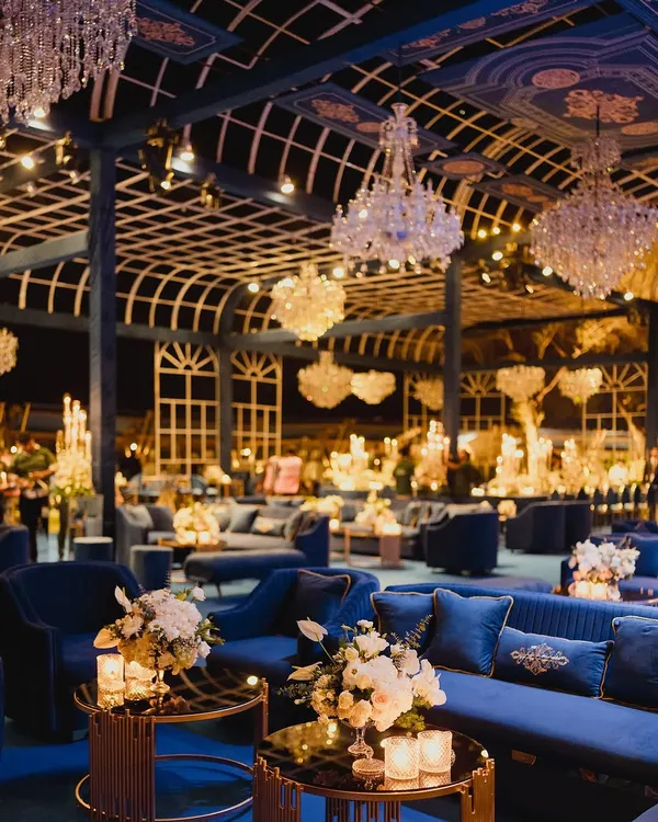 A wide view of the magnificent gala, showcasing the seamless integration of luxurious blue velvet seating, ambient candlelight, and grand floral arrangements. Every element is designed to create a cohesive and opulent environment for a high-end corporate event.