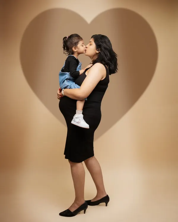 A love that grows with every heartbeat. This portrait captures a mother holding not just her little one, but also the new life growing within her, all framed by a heart of light.